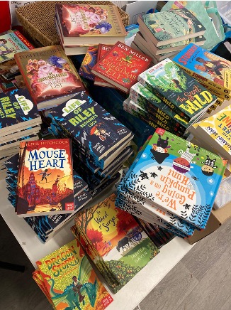 Table stacked with various colorful children's books including 'Mouse Heart,' 'Life of Riley,' 'Dragon Storm,' and 'We're Going on a Pumpkin Hunt'.
