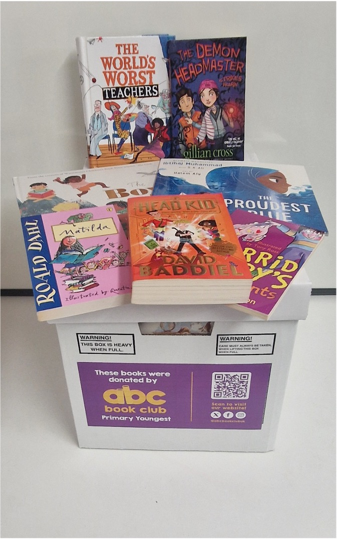 A box labeled 'abc book club Primary Youngest' filled with various children's books including 'The World's Worst Teachers,' 'The Demon Headmaster,' 'Matilda,' 'Head Kid,' and 'The Proudest Blue.'