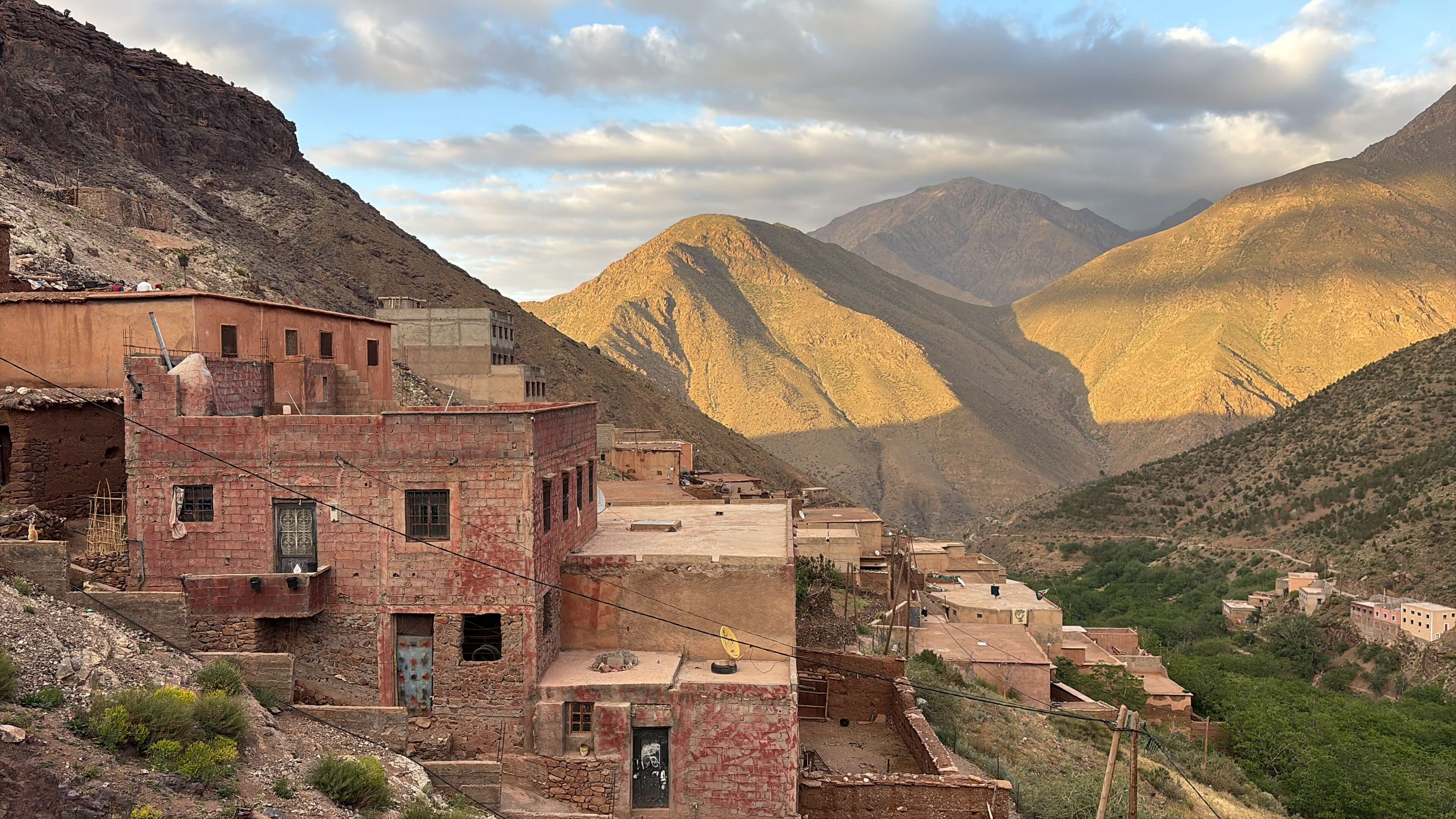Mountain village with clustered mud-brick houses under a partly cloudy sky during golden hour.