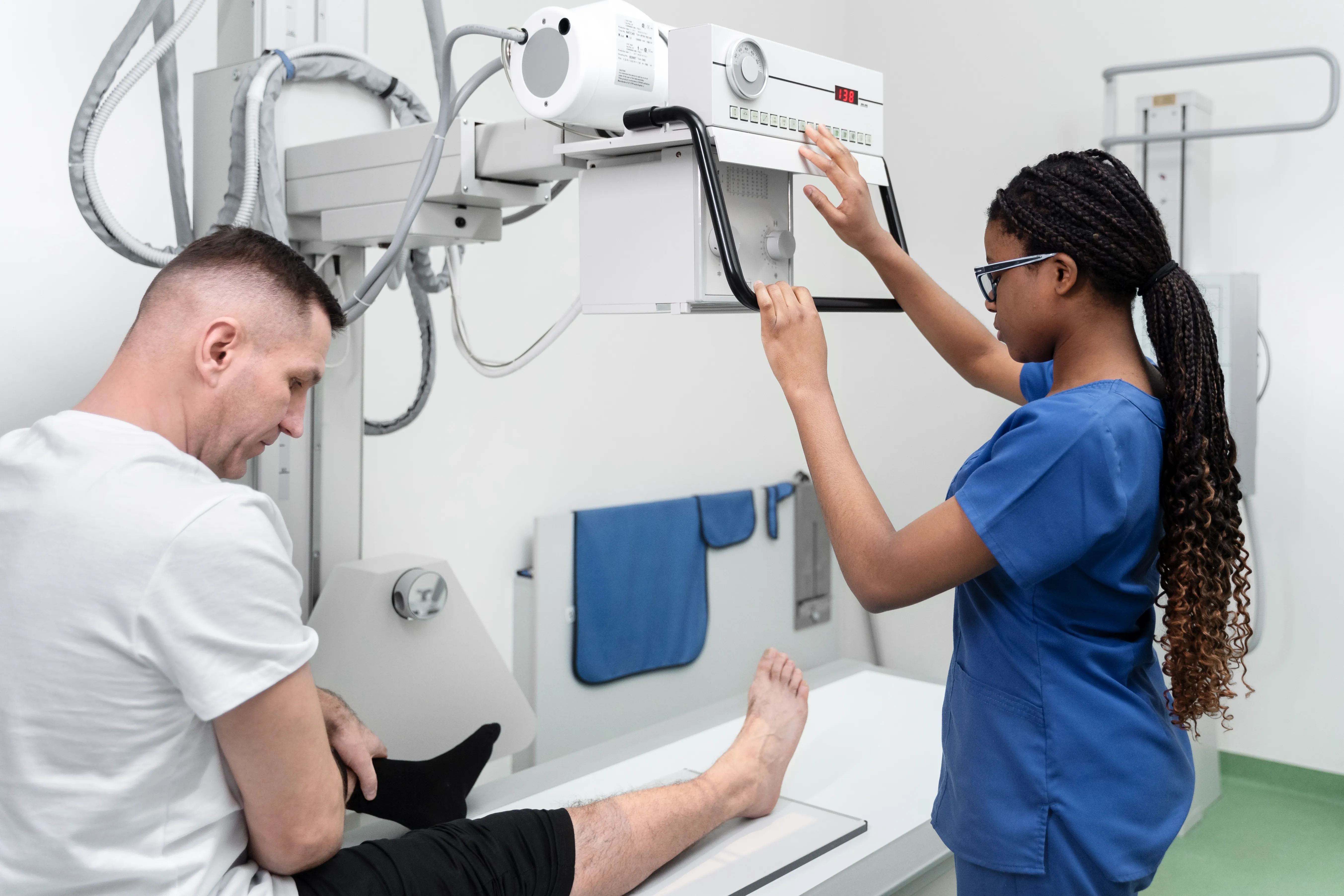 Young woman with glasses doing a radiation scan of man's leg in hospital o setting.