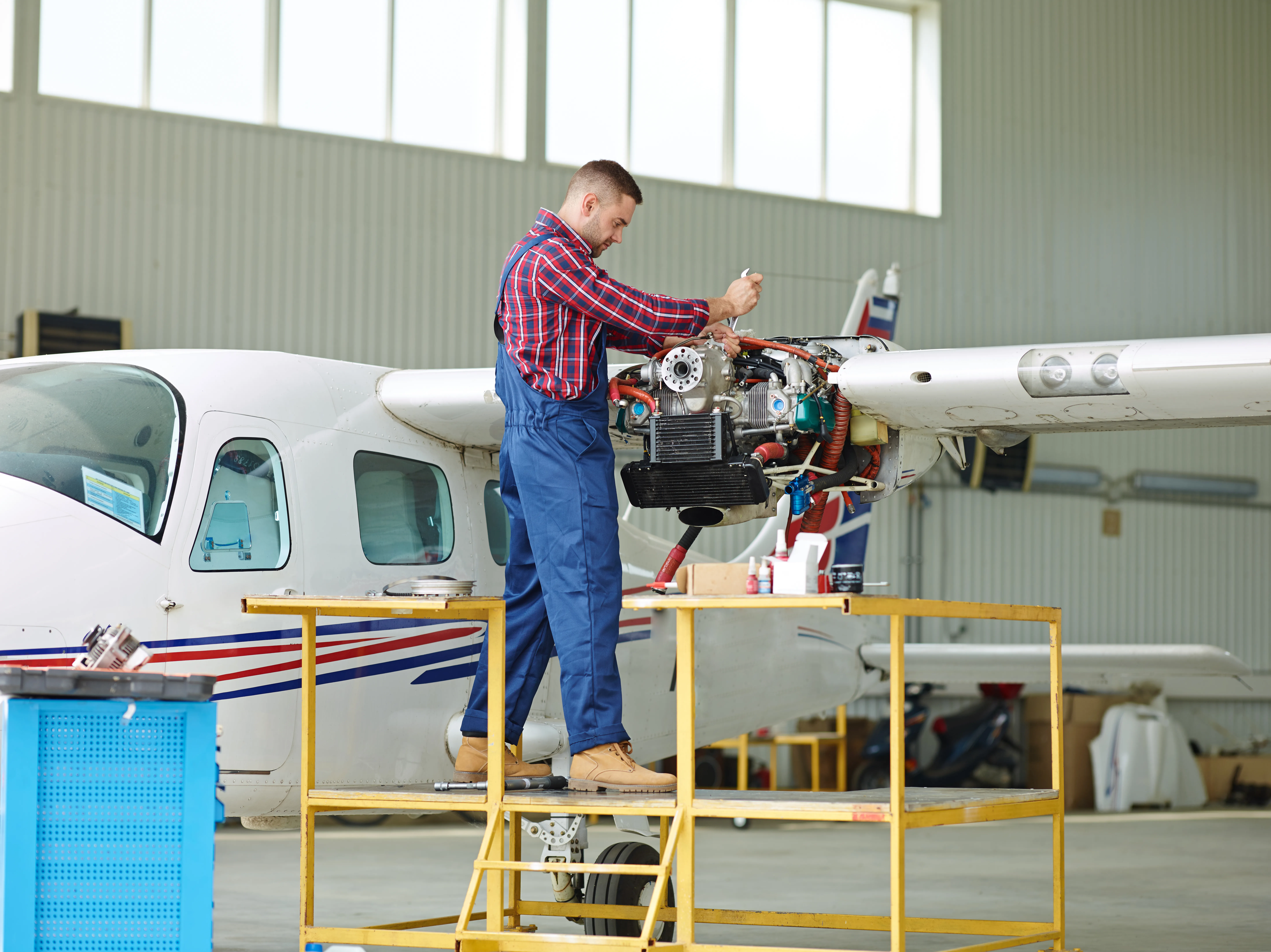Man working on a disassembled plane engine using a wrench on ladder.