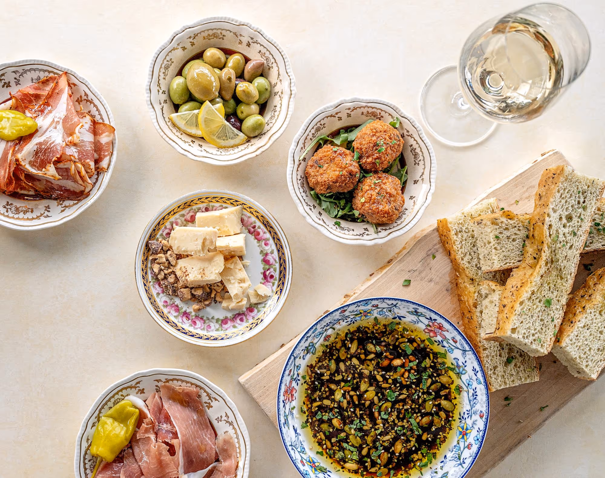 A variety of cheese, olives and cold cuts plated on a clean table, set with a glass of wine and focaccia bread.
