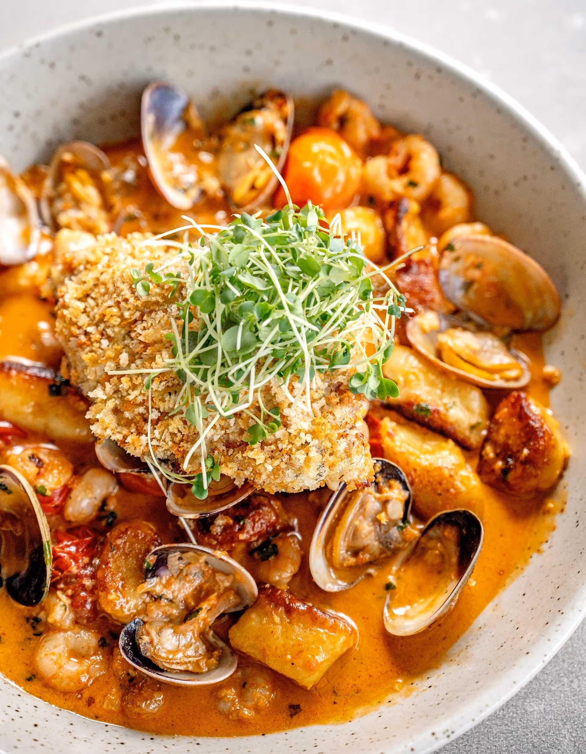 A beautifully plated dish of lemon & dill crust lingcod, baby shrimp, grape tomatoes, clams, mussels, house-made gnocchi, rosé sauce.