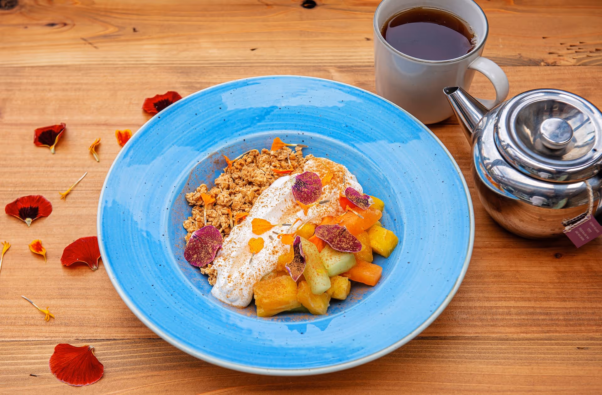 A blue bowl with house-made maple granola, seed blend, honey & vanilla yogurt, and freshly cut fruits.