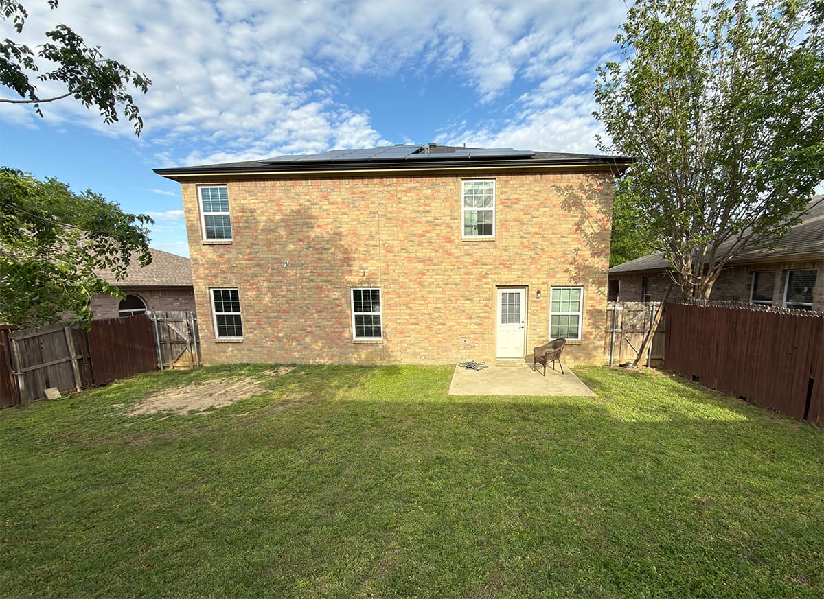 The back of a brick house in the backyard with an empty patio.