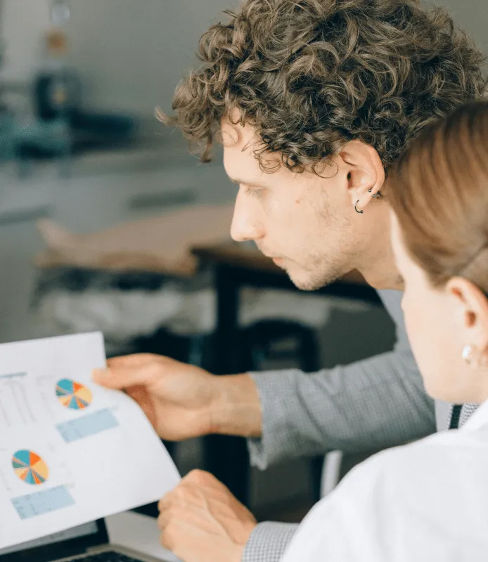 Two employees analyzing a sheet with stats 