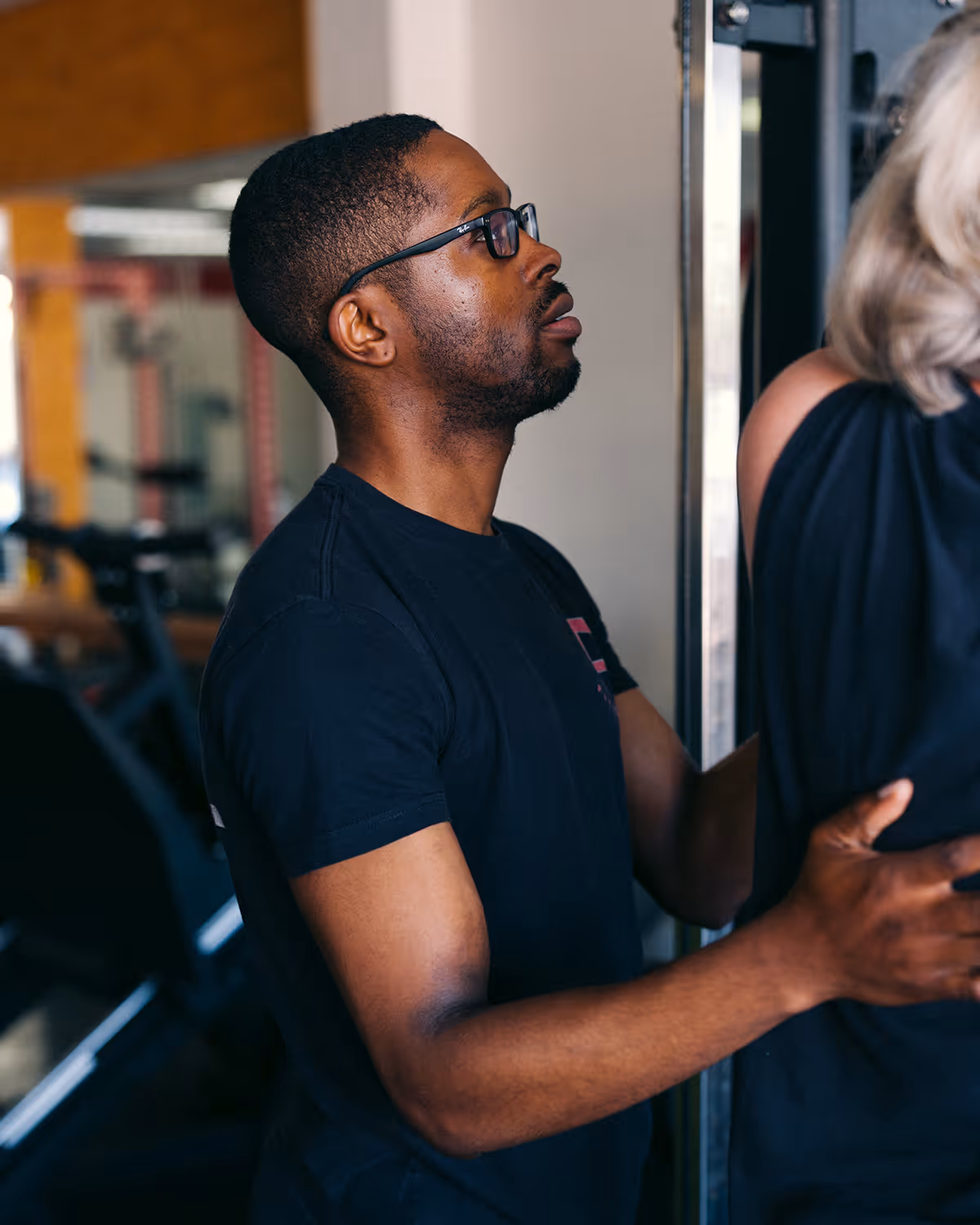 Joshua Balogun, Master Trainer, assisting a woman with blonde hair in black clothing at Fit Factor in Memorial City Houston.