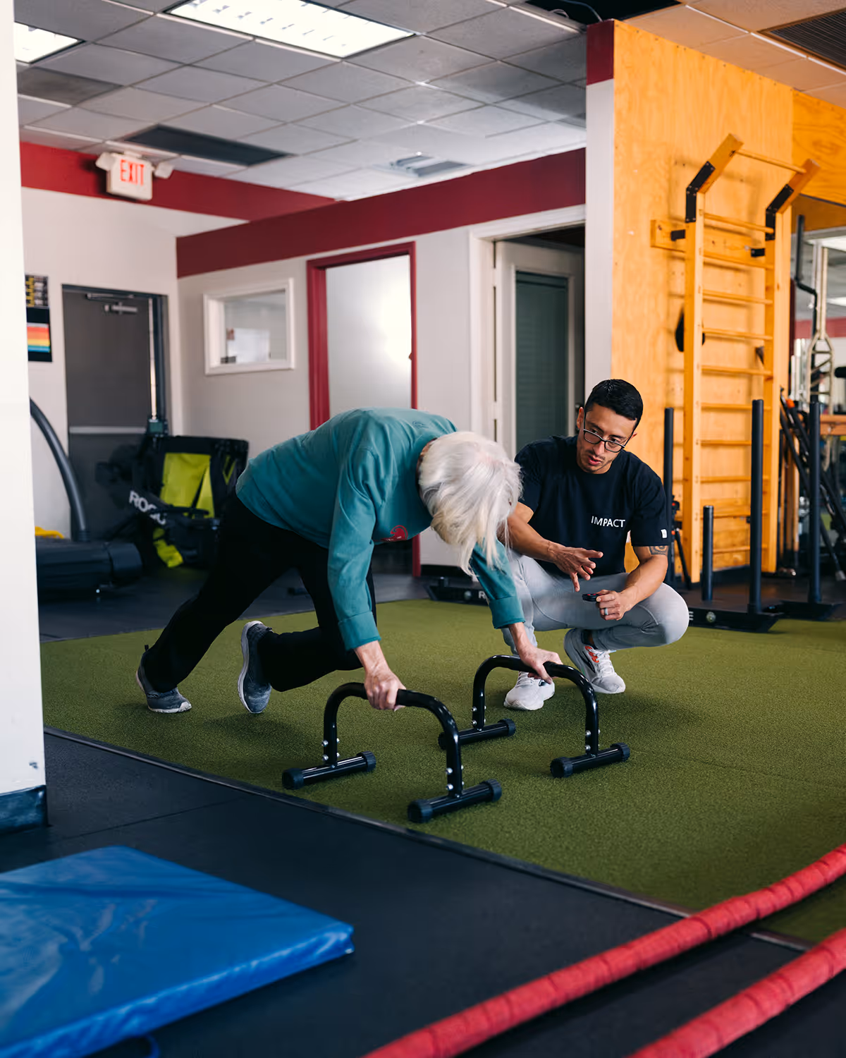 Senior woman exercising with push-up bars guided by Fabian Salazar, Owner & Master Trainer, at Fit Factor in Memorial City Houston.