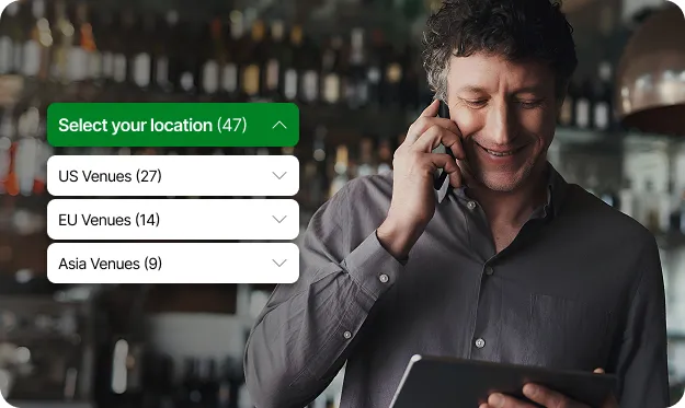 Homme souriant parlant au téléphone tout en tenant une tablette, avec une interface utilisateur superposée montrant les options de sélection de l'emplacement des lieux pour les États-Unis, l'UE et l'Asie.