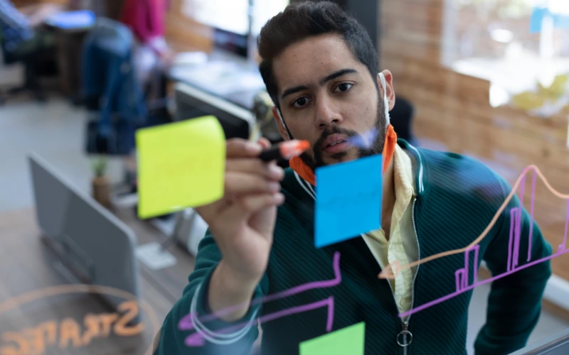 A focused professional writes on a transparent board with colorful charts and sticky notes, representing strategic planning. The image illustrates best practices for AI event marketing strategies, emphasizing organization and data-driven decision-making.