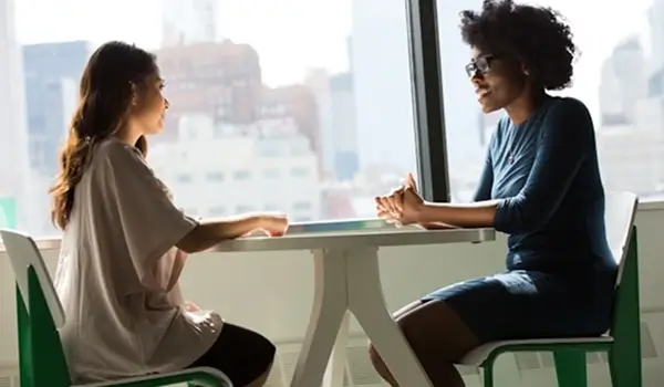 Two women sitting at a table engaged in conversation at a professional networking event.
