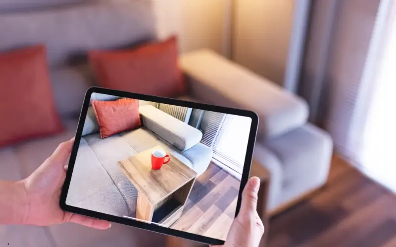 Person using a tablet to view augmented reality furniture placement in a living room.