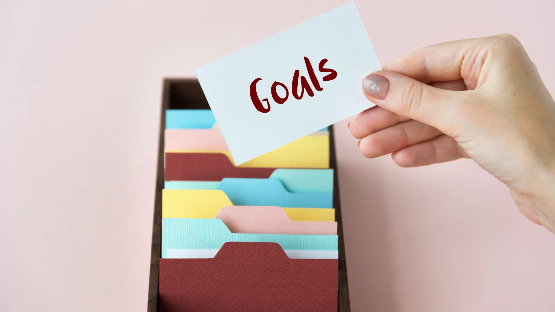 Hand holding a goals card over colorful folders symbolizing step one of How to Host a University Virtual Career Fair. 