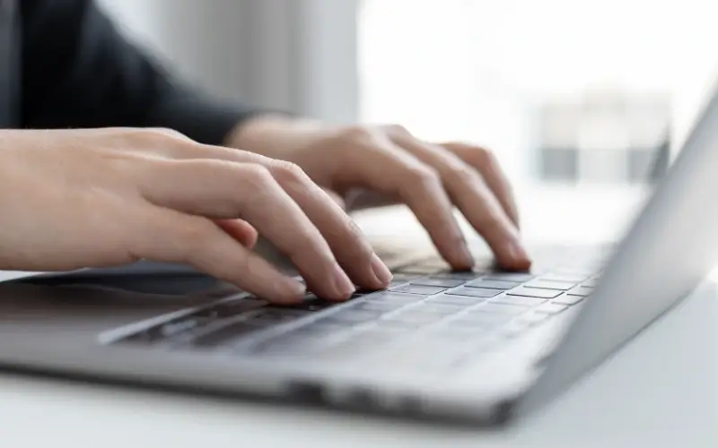 Person typing on a laptop, drafting a press release for an upcoming event.
