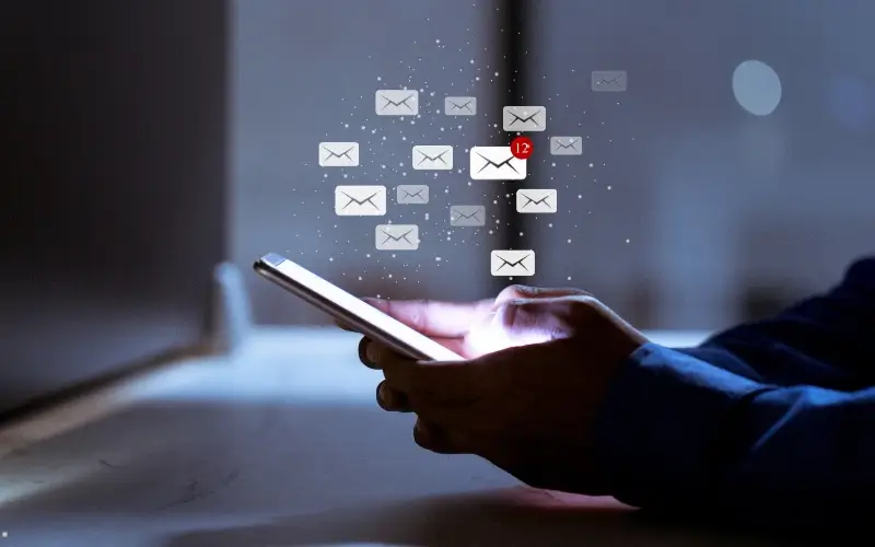 Hands using a smartphone while multiple email icons appear above, symbolizing event press release distribution.