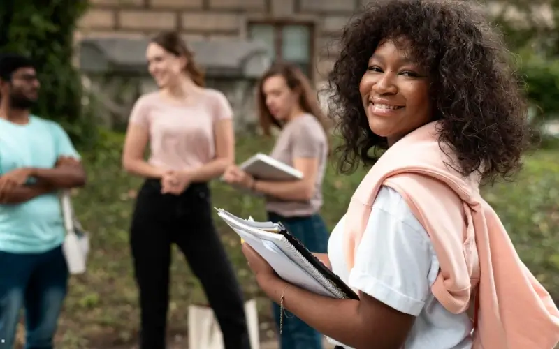 A group of diverse Gen Z students holding notebooks and discussing future plans, representing the shift toward independent, digital-first exploration that supports virtual education fairs.
