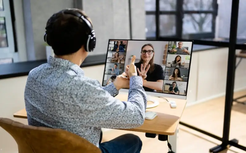 Student attending a virtual education fair through a video call, engaging in a live discussion with multiple university representatives using accessible online features and sign language.