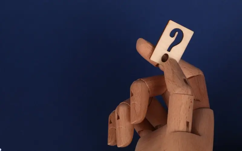 A wooden figure holding a card with a question mark, representing the use of AI to analyze data, uncover insights, and measure what matters in event performance.