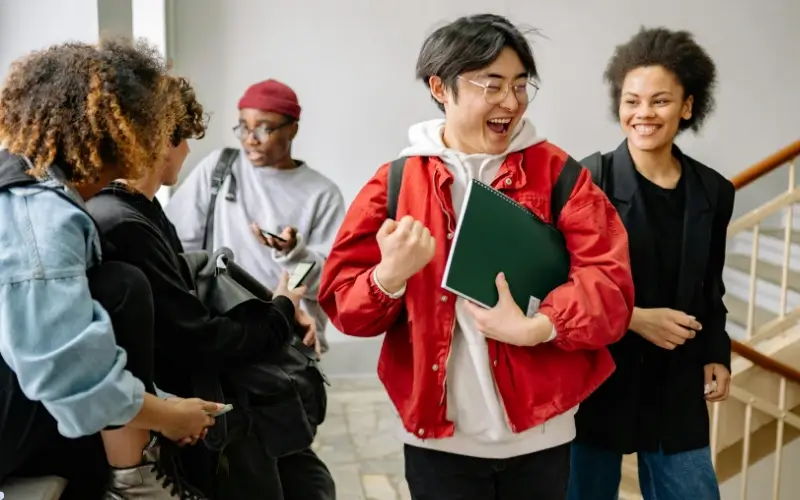 Diverse group of teens talking and smiling in a school hallway, representing a wide range of icebreaker questions for teens across different situations.