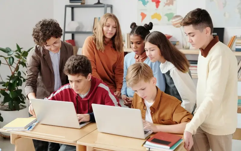Group of teenagers working together on laptops in a classroom setting, representing collaborative activities and crafting effective icebreaker questions for teens.