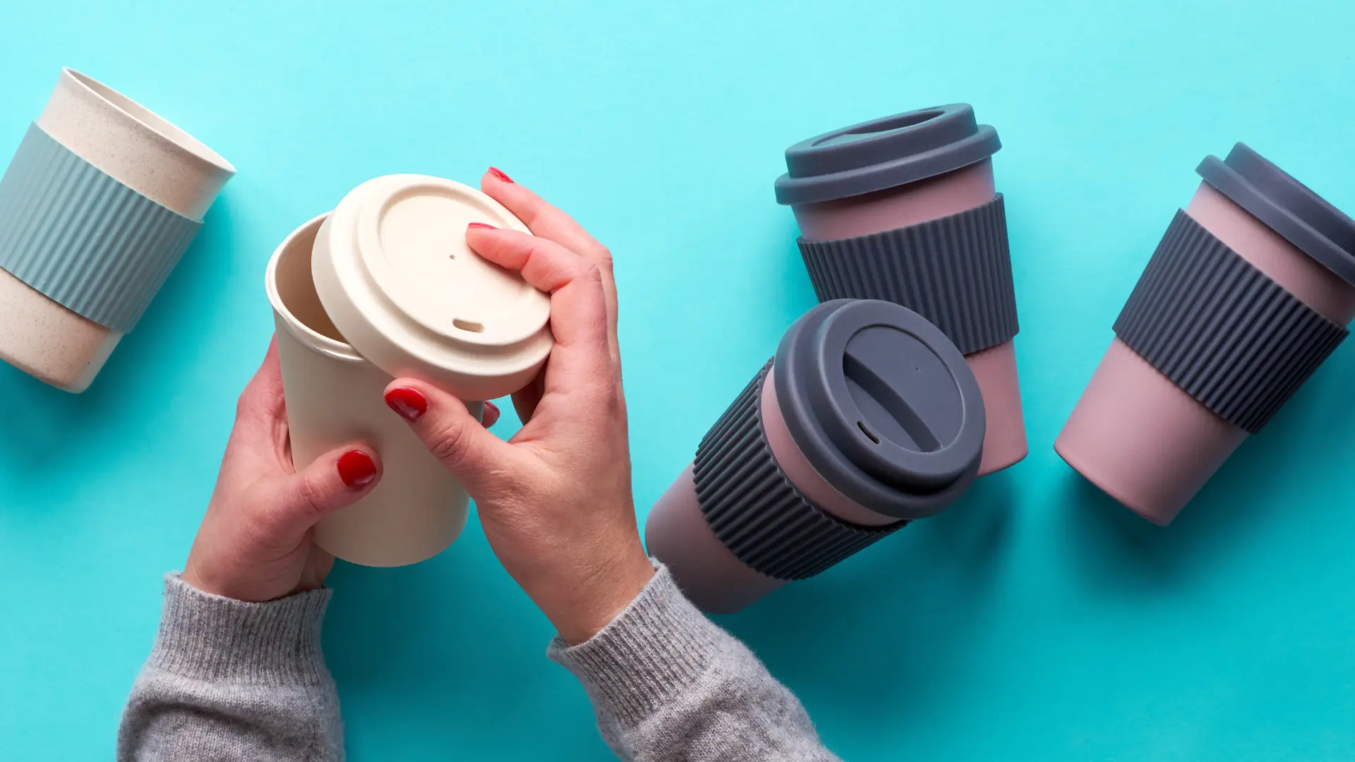 Reusable coffee cups on a teal background, a sustainable option for career fair giveaway ideas.
