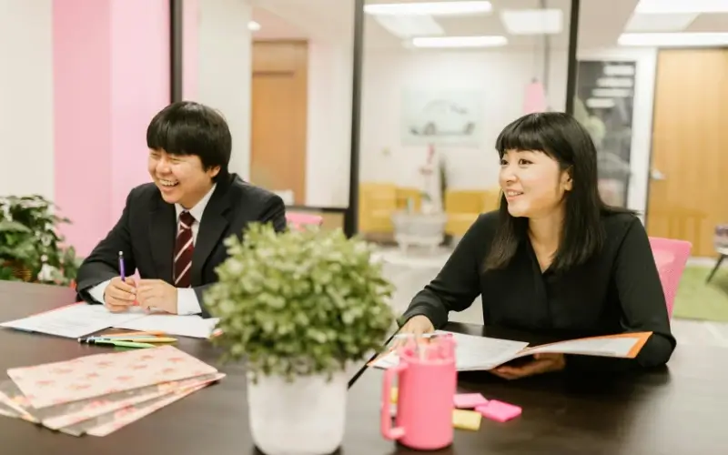 A man in a suit and a woman in a black blouse sitting at a table during an interview, smiling and looking toward a candidate off-camera.
