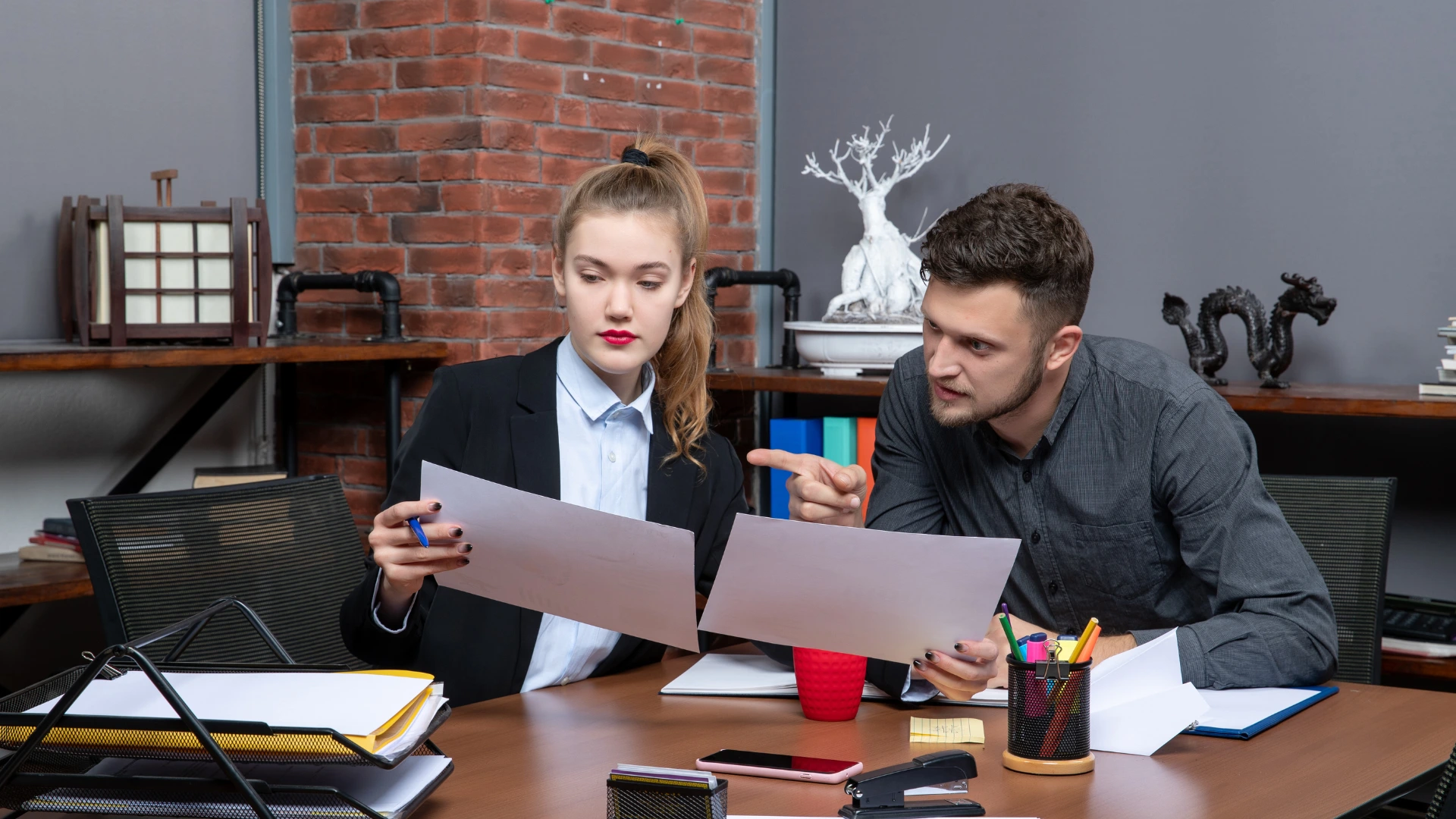 Two colleagues reviewing printed documents together at a desk in an office setting.