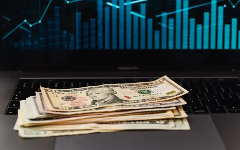 Laptop displaying financial graphs with cash on the keyboard, representing revenue tracking, pipeline growth, and sponsorship ROI performance.
