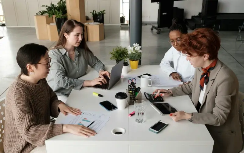 A diverse group of professional employers collaborating around a table with laptops and documents, representing a curated mix of industry tracks.