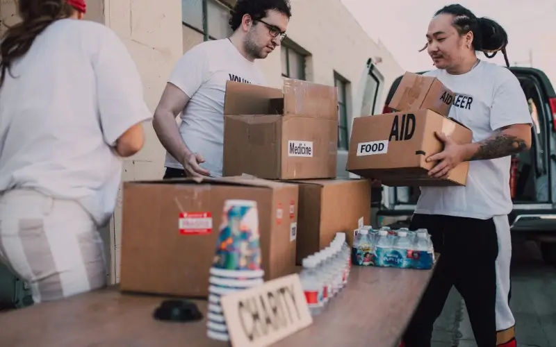 Volunteers wearing matching t-shirts sorting and packing boxes labeled for food, medicine, and charity aid.