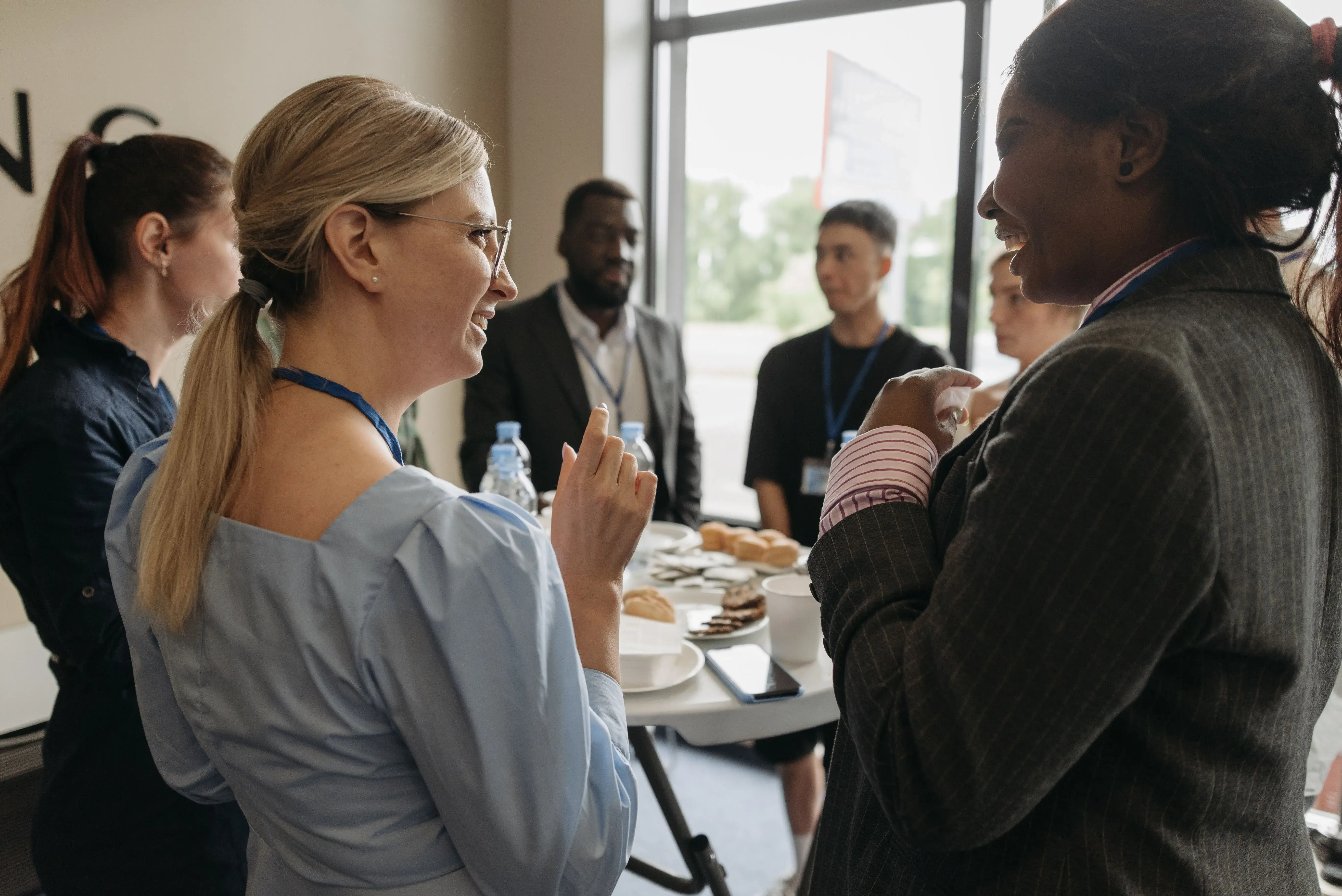 Attendees wearing lanyards conversing around a refreshment table during an in-person business networking break.