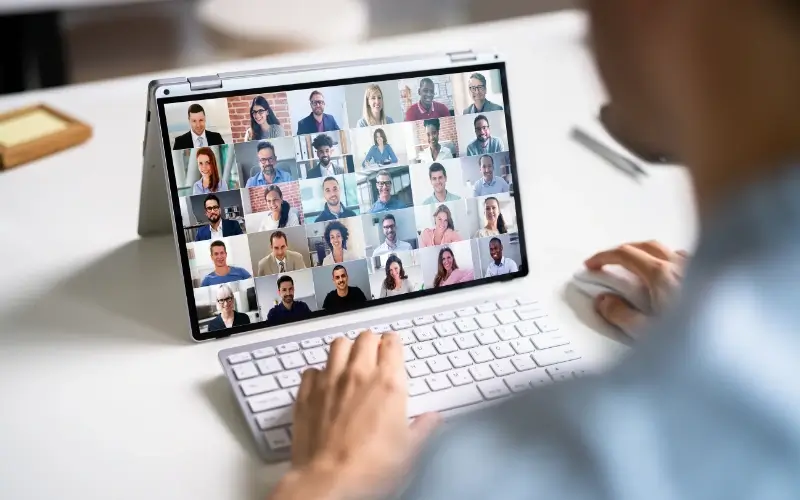 Person typing on a laptop displaying a grid view of diverse participants in a virtual meeting.