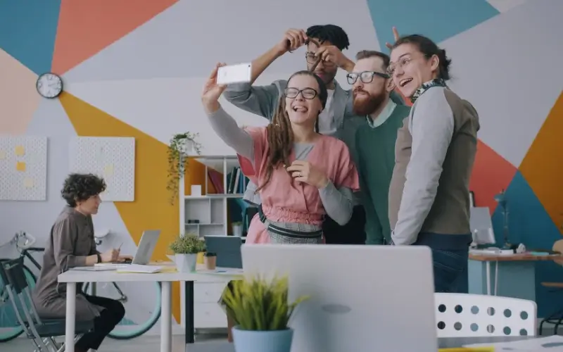 Four coworkers taking a group selfie together in a colorful office.
