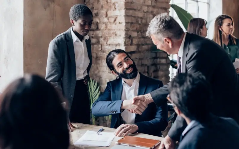 Colleagues talking during a professional meeting, with two people shaking hands.
