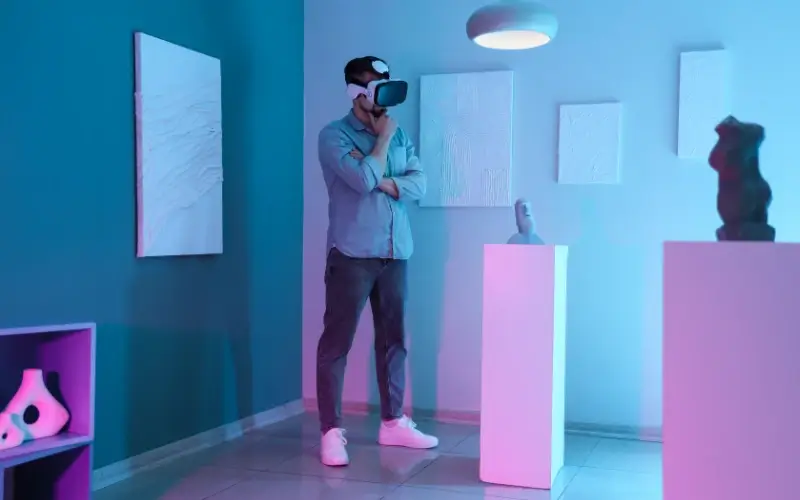 Man wearing a VR headset exploring a virtual art gallery with sculptures and wall art illuminated by neon lighting.