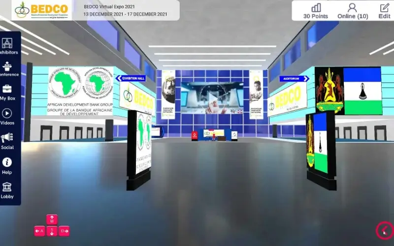 3D virtual exhibition center layout showcasing promotional sponsor banners, direction signs to an auditorium, and first-person navigation controls.