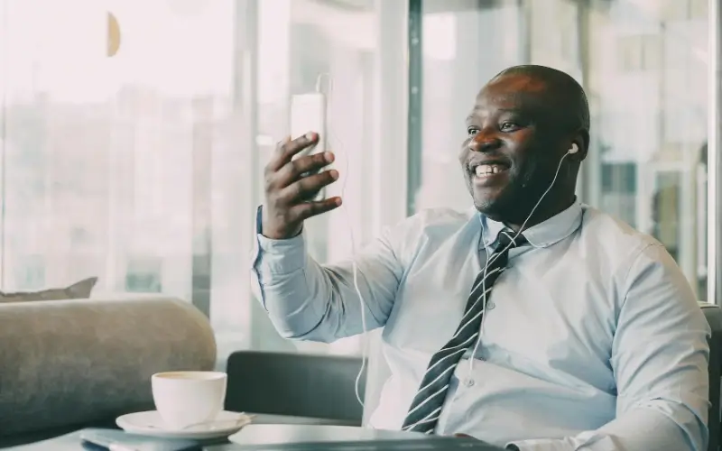 A professional joins a video call on a smartphone while relaxing in a bright office setting.