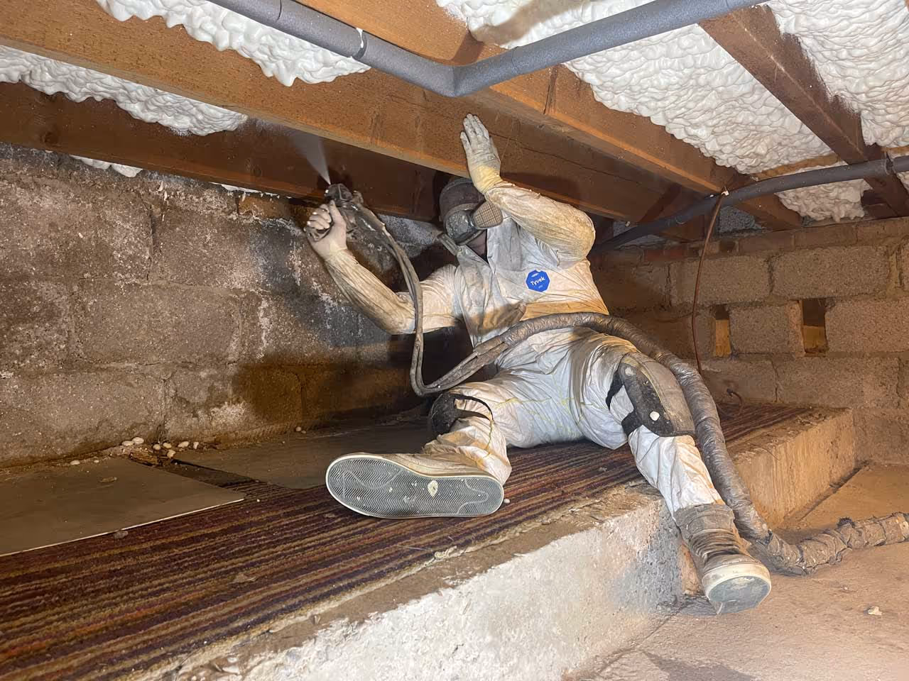 Someone operating a spray foam gun spraying onto flooring joists