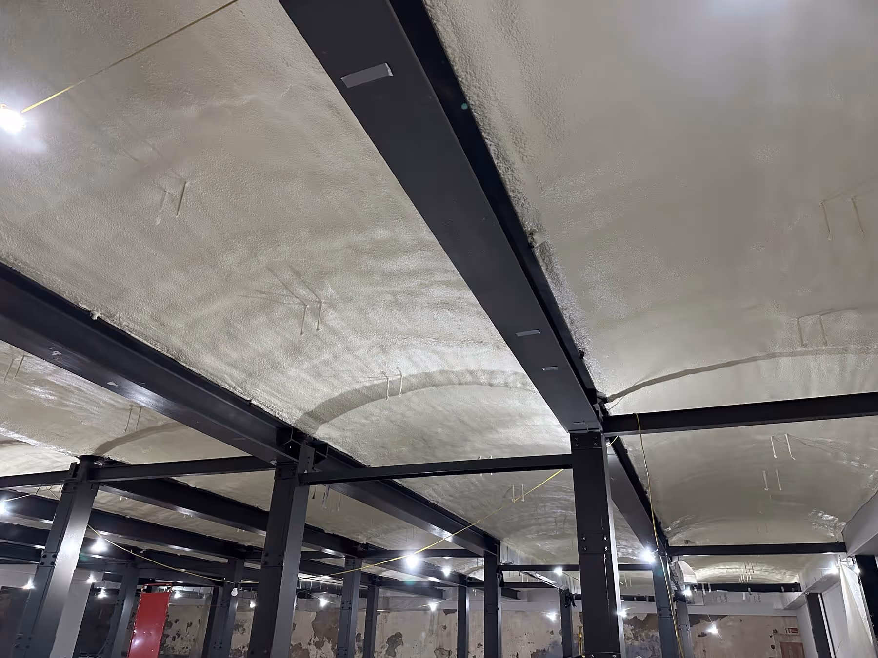 The image shows a building interior with steel beams and white arched ceilings.