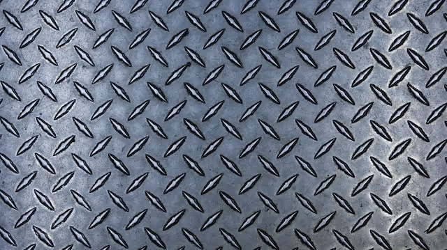 A photo of a metal surface with a diamond plate texture, featuring raised, repeating diamond shapes.