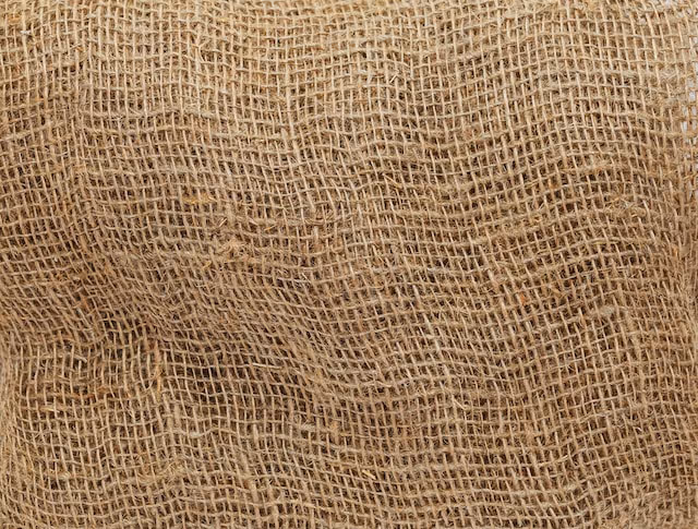 The image shows a textured close-up of woven burlap fabric with a natural, earthy tone.