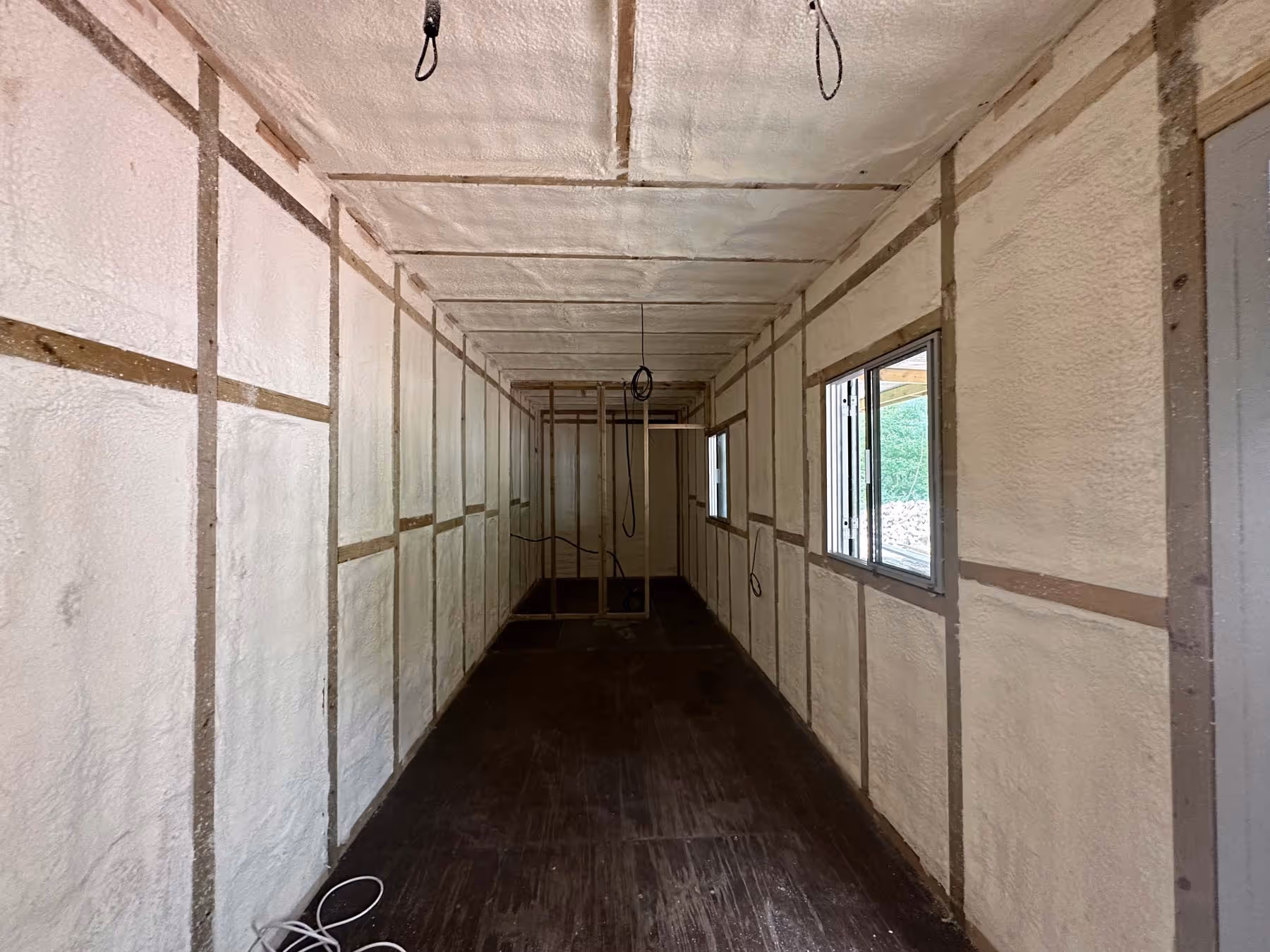 A photo of an empty, narrow room with insulated walls and two windows on one side.