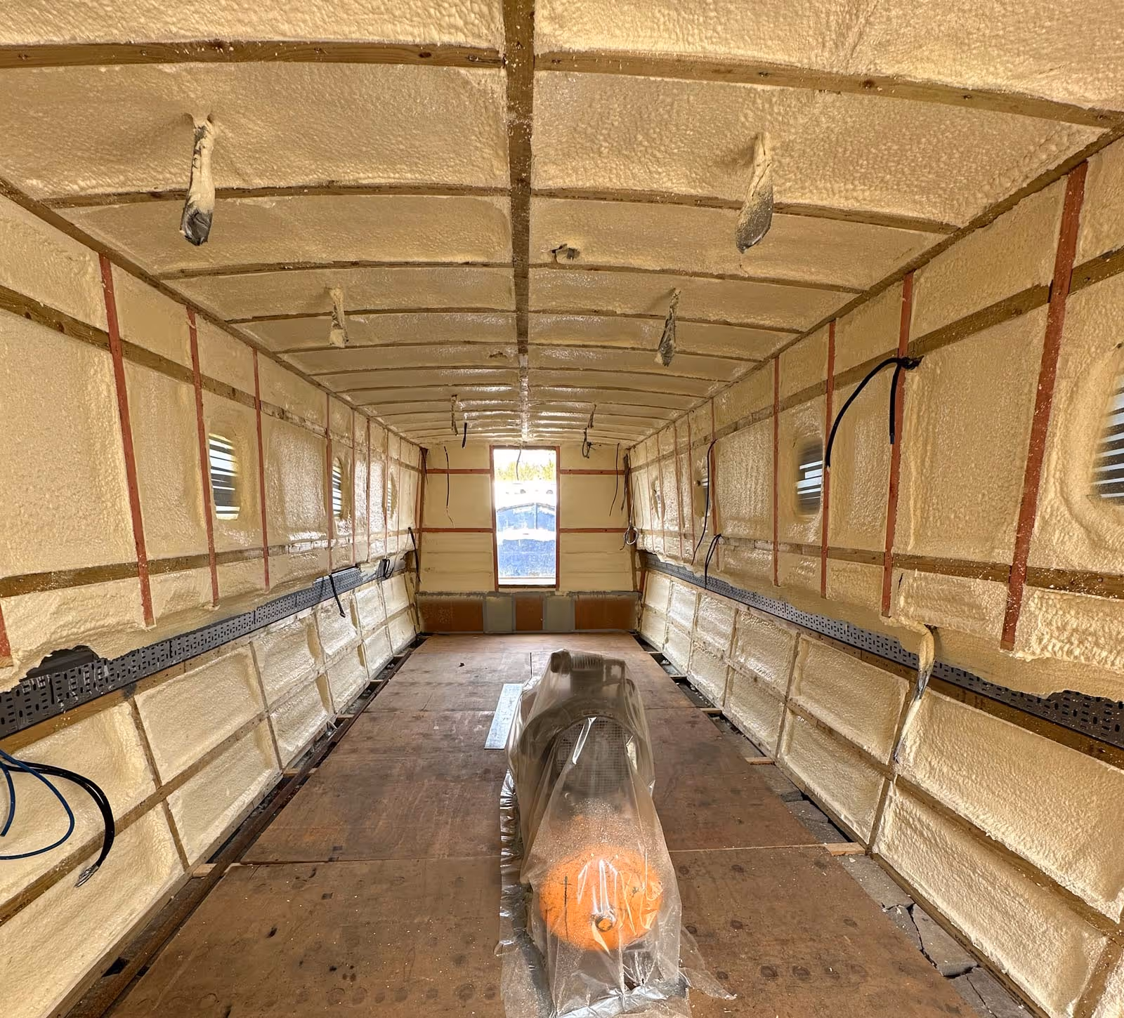 Interior view of a stripped-down vehicle or container, insulated walls and ceiling, with some visible wiring.