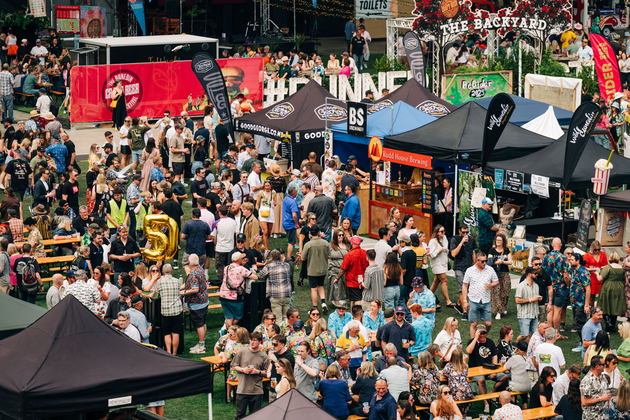Crowd at outdoor beer festival with vendor tents, picnic tables, and large event signage.