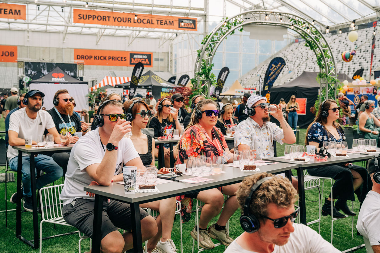 People wearing headphones seated at tables tasting drinks at an indoor festival event.