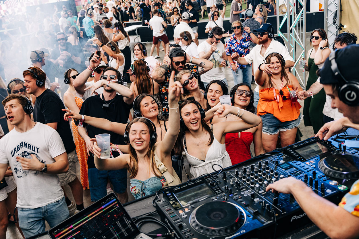 Crowd enjoying outdoor silent disco event with DJ and people dancing wearing headphones.