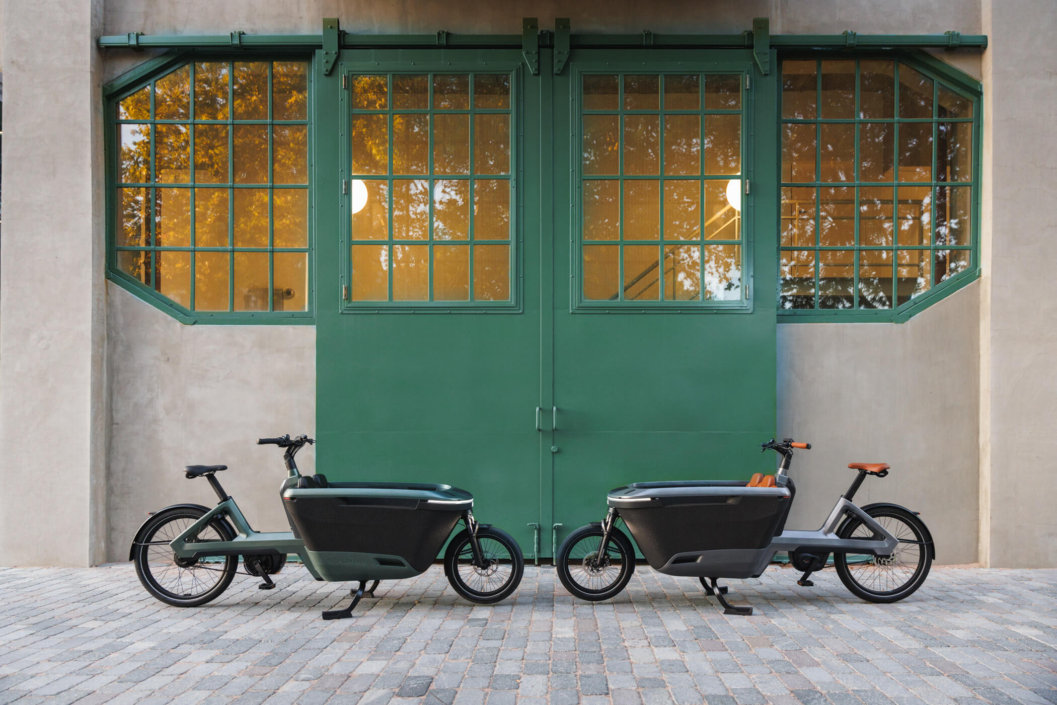 Schönes Foto von 2 Lovens Explorer E-Cargobikes vor einem grünen Tor.