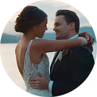 Bride and groom embracing and smiling at each other outdoors during sunset by a body of water.