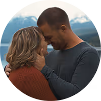 Couple embracing closely with foreheads touching against a backdrop of mountains and water.