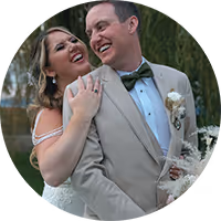 Bride playfully hugging groom from behind outdoors, both smiling happily.